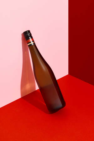Bottle of wine leaning on the wall. Alcoholic drink on red and pink creative background with deep shadowsの写真素材