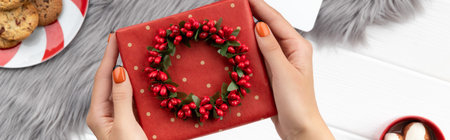Womans hands holding gift with cocoa and cookies on furry background