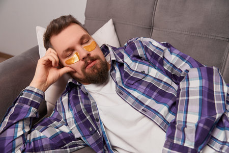 Man in purple shirt with eye patches sleeping on the couch. Self care routine