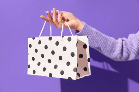 Womans hand holding white paper shopping bag on purple background. Shopping sale delivery conceptの写真素材