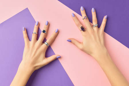 Beautiful womans hands in with purple fashionable spring nail design on pink purple backgroundの写真素材