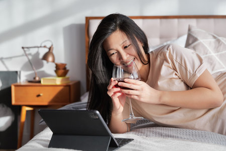 Happy beautiful woman in casual clothes talking on video call on digital tablet lying on the bed. Work from home education onlineの写真素材
