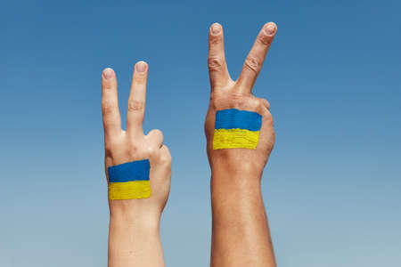 Womans and mans hands with painted ukrainian flag peace sign against the blue sky. Stop warの写真素材