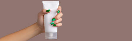 Womans hand holding white tube on brown begie backgroundの写真素材