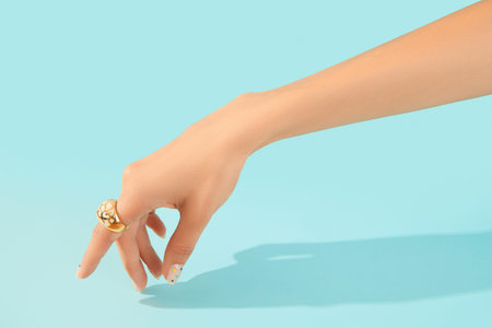 Beautiful groomed womans hand with fashionable ring on blue background