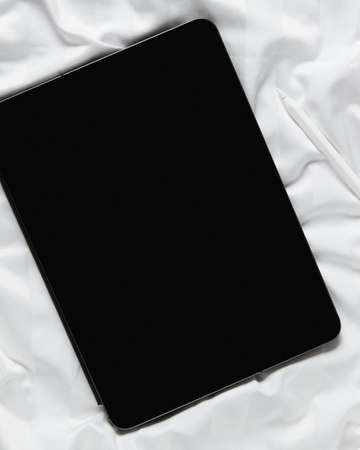 Flat lay top view blank screen digital tablet on white bed. Home office workspaceの写真素材