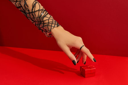 Beautiful groomed womans hands with gift box on red background. Halloween shopping sale concept