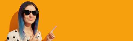 Young adult woman with blue hair on yellow background. Smiling girl pointing and looking at camera