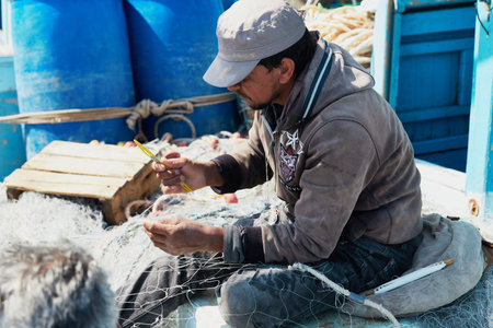 HURGHADA, EGYPT - FEBRUARY 19, 2022: Local fisherman repairs fishnets on the boat and getting their...