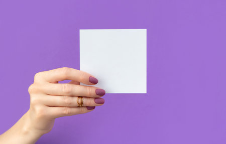 Beautiful womans hand with manicure holding postcard on purple backgroundの写真素材