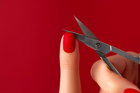 Manicured female hand with scissors on red background. Red matt nail designの写真素材