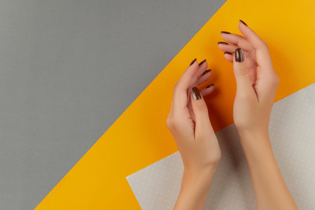 Beautiful groomed womans hands with brown nail design on creative colorful backgroundの写真素材