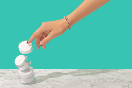 Womans hand touch white jars on turquoise backgroundの写真素材