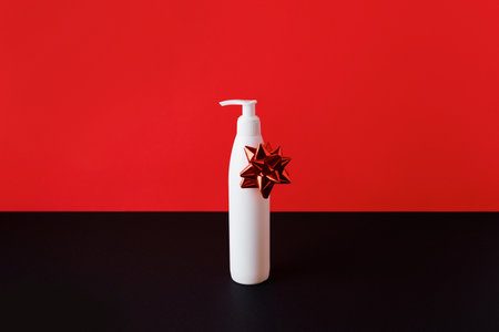 White bottle of cosmetics cream or cleansing foam with bow on red-black background. Sale conceptの写真素材