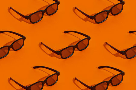 Pattern made with black plastic 3d glasses on orange background