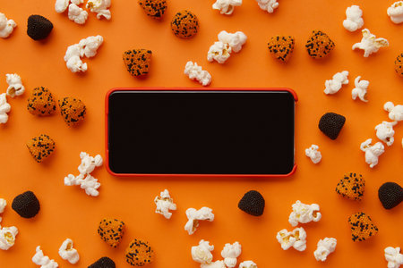 Smartphone, box of popcorn and gummies on an orange backgroundの写真素材