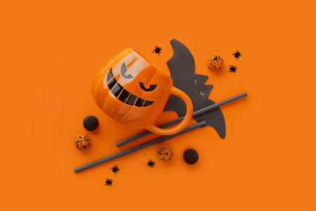 Pumpkin cup, gummy, straws, bat napkin on orange background. Halloween celebration conceptの写真素材