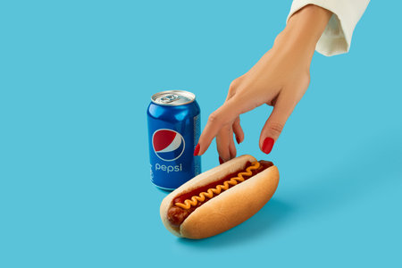 KIEV, UKRAINE - SEPTEMBER 16, 2021. Traditional hot dog and Pepsi cola with womans hand on blue...