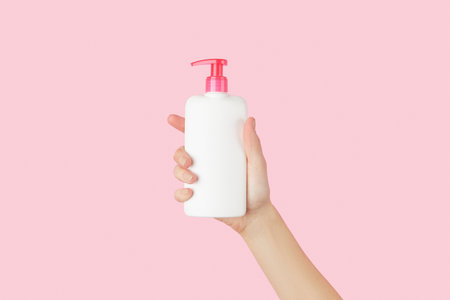 Womans hand holding white bottle on pastel pink backgroundの写真素材