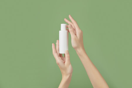 A womans hands holding a white cosmetic bottle on a green backgroundの写真素材