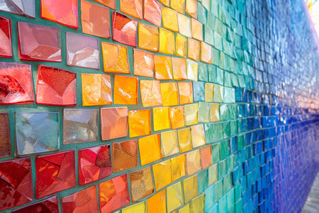 Vibrant mosaic wall of red, orange, yellow, green, and blue tiles arranged in a gradient patternの素材