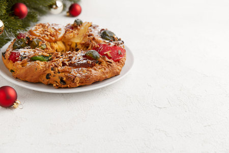 A wreath shaped cake with candied fruit and nuts, displayed with Christmas ornaments and a treeの写真素材
