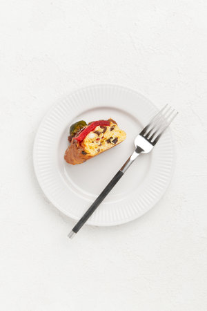 A slice of festive cake with candied fruit and nuts on a white plate with a fork placed beside itの写真素材