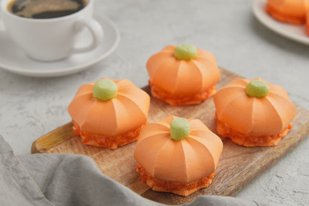 Four pumpkin shaped desserts with green tops placed on a wooden board next to a cup of coffeeの写真素材