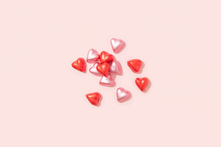 Wrapped heart-shaped chocolates in red foil on a pink background with deep shadows
