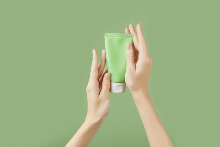 A womans hands holding a tube of lotion on a green background. Body careの写真素材