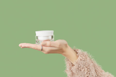 A woman's hand in a sweater holds a jar of cream on a green background.の写真素材