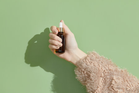 A womans hand holding a brown bottle of serum on a green backgroundの写真素材