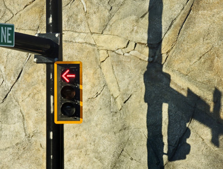 Streetlight with red left turn arrow pointing away from its shadow on nearby retaining wall.の写真素材
