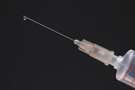 medical syringe with a needle and a droplet on dark background