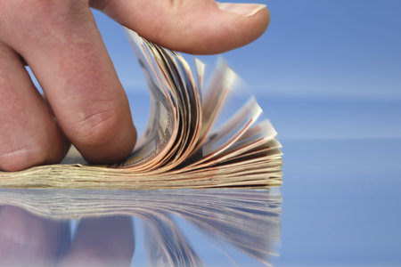 Hand counting money, closeup on blue background with reflections
