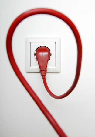 Red power cable plugged in electric outletの写真素材