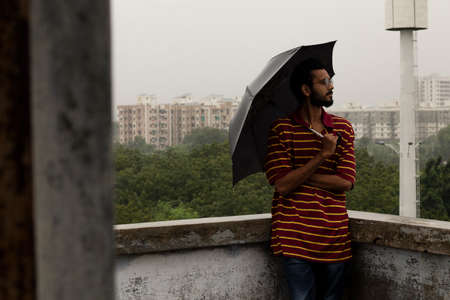 Indian man standing in rain with black umbrellaの写真素材
