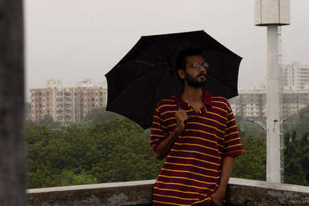 Indian man standing in rain with black umbrellaの写真素材