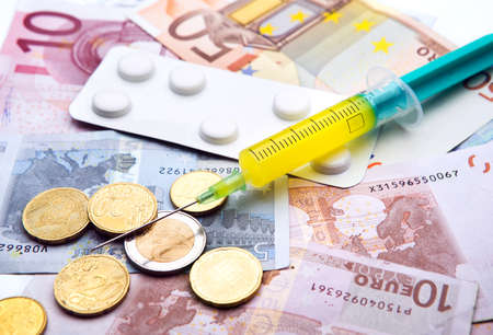 medical syringe and strip of tablets lying upon european currency bills and coinsの写真素材