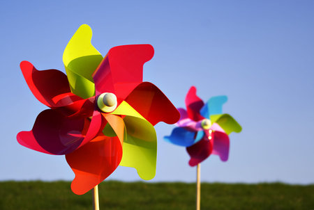 two colorful pinwheels in bright sunlight on a meadow, blue sky