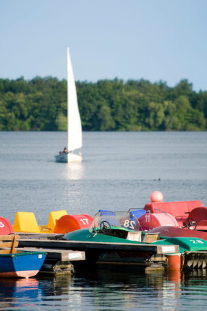 jetty with colorful pedalos, sailboat in backgroundの写真素材