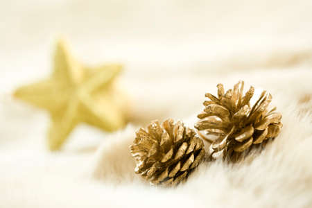 christmas decoration - golden pine cones on fur, out of focus star shape in back, suitable as background imageの写真素材