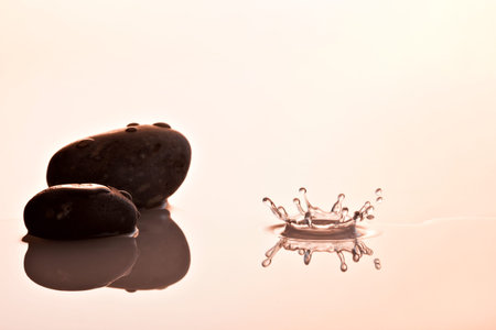 waterdrop impact making crown-shaped splash near two pebbles の写真素材