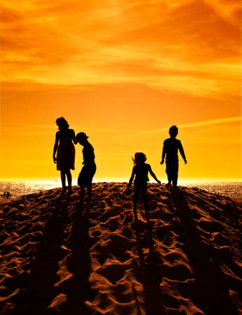four children playing on a sand hill at the beach in sunset, high contrastの写真素材