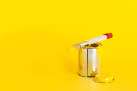 open can of yellow paint with brush on top on yellow backgroundの写真素材