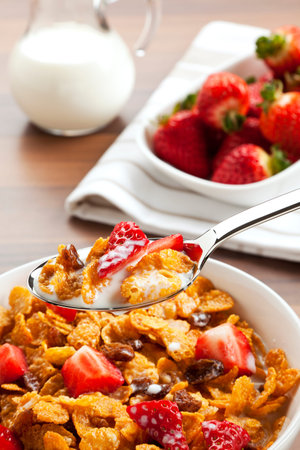 spoonful of cereals and fruits with milk above full bowl on table, strawberries and milk in...