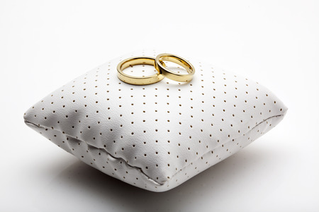 golden wedding rings on small white leather cushionの写真素材