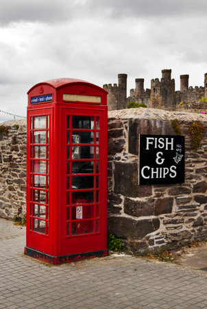 Typical place in Britain - red telephone booth, fish and chips directional sign, old castle, grey skiesのeditorial素材
