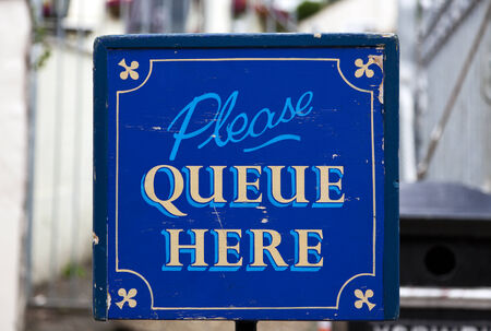 old wooden sign saying "Please queue here"の写真素材