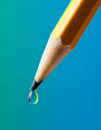 Water drop with rainbow colored refraction clinging on the tip of a pencilの写真素材